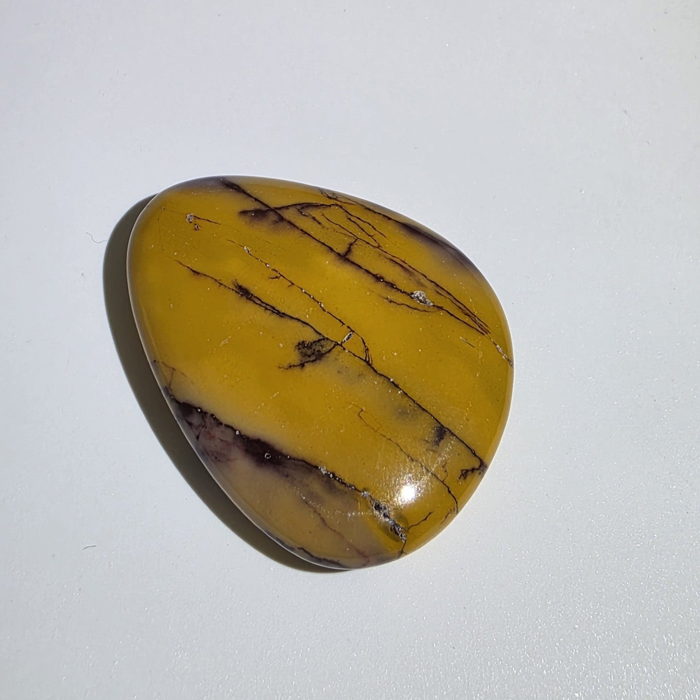 Mookaite palm stone on white background – natural Australian jasper in rich earthy tones of burgundy, cream, and yellow