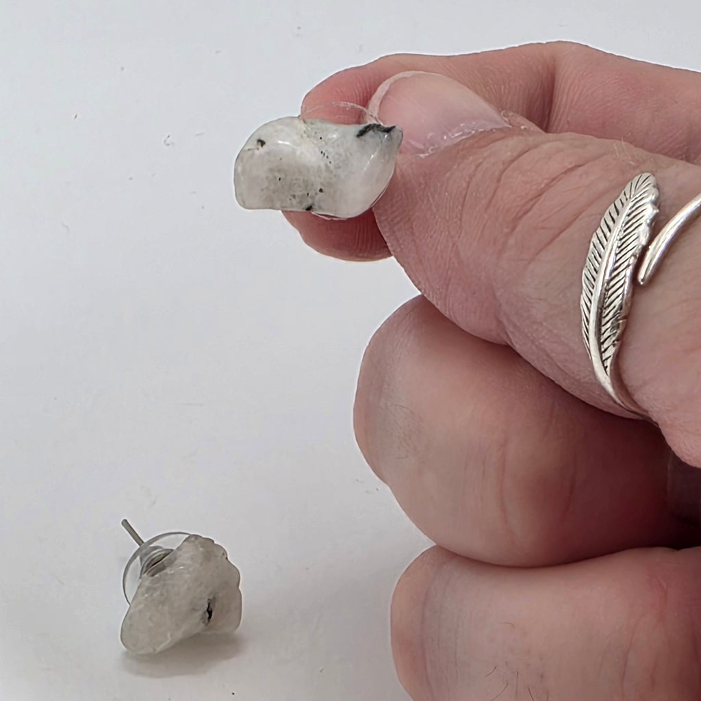 Close-up of a hand holding a Moonstone earring on a white background