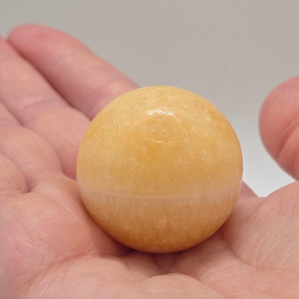 Orange calcite sphere 35mm held in a person's hand – warm orange crystal for sacral chakra energy
