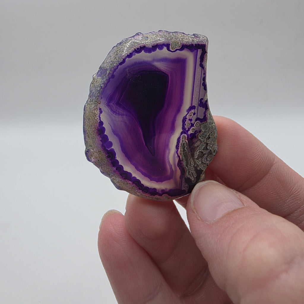 Rainbow agate slice held in a person's hand – small colourful crystal slab for display or grid work