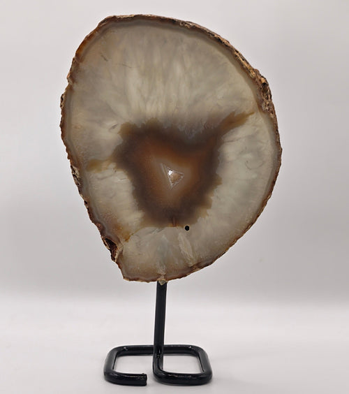 A polished agate geode slice with a brown and cream interior, displayed on a black metal stand against a plain white studio background.