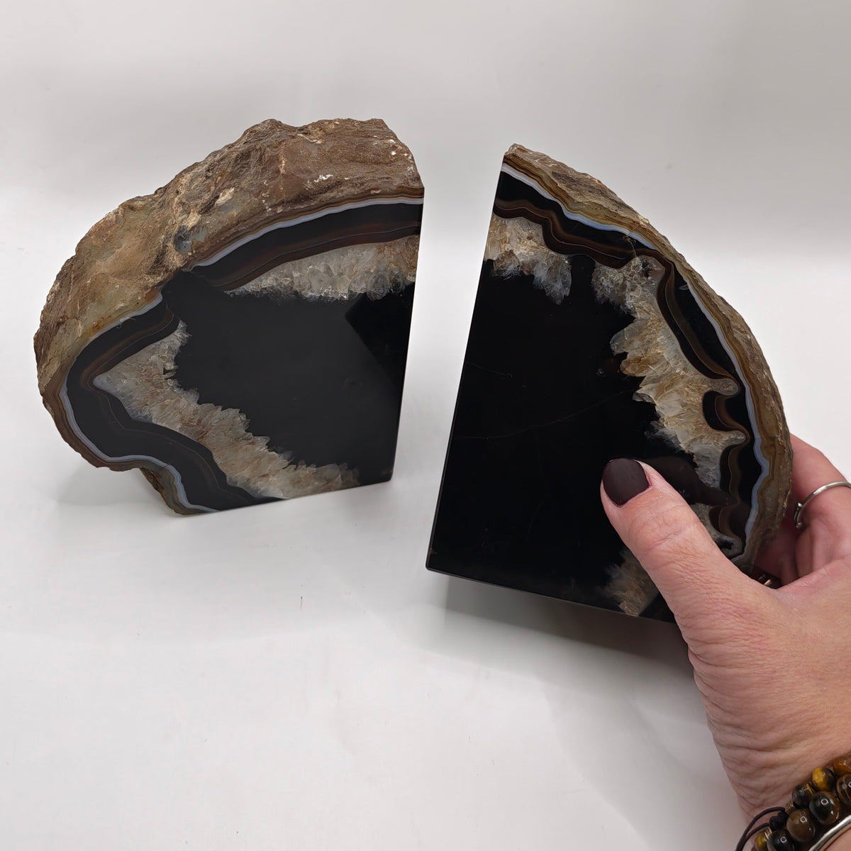 Two polished agate geode bookends on a white background, with a hand holding one to show its depth and texture.