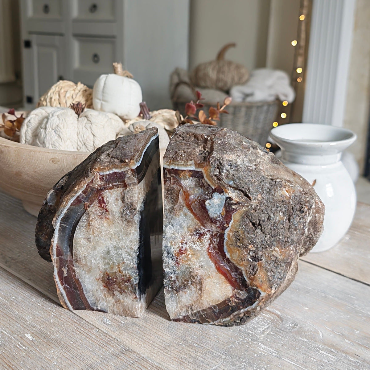 The back displayed on a rustic wooden table in a styled home interior, with pumpkins, a white cabinet, and warm string lights in the background.