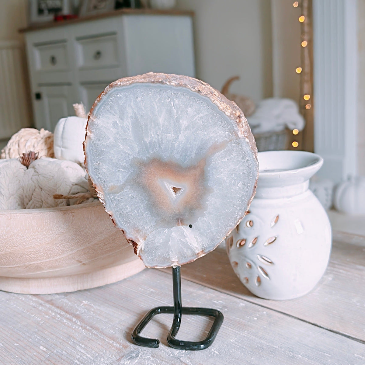 The Back of the  polished agate slice with a natural wood edge and pale cream interior, displayed on a small black stand on a rustic wooden table in a softly lit room.
