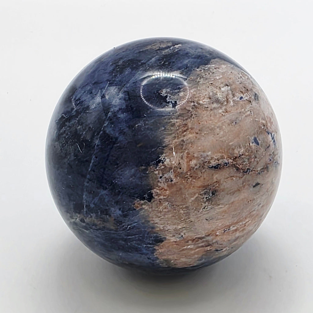 Polished 4cm sodalite crystal sphere with deep blue colour and white veining on white background