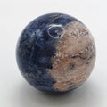 Polished 4cm sodalite crystal sphere with deep blue colour and white veining on white background