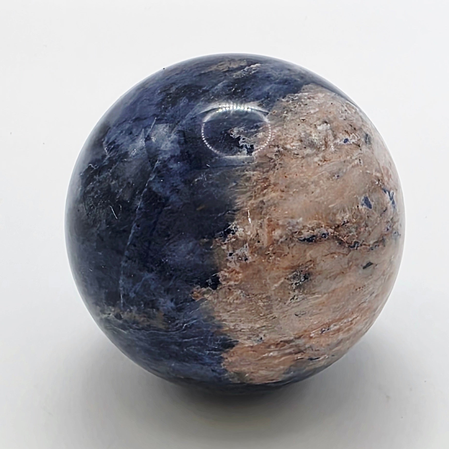 Polished 4cm sodalite crystal sphere with deep blue colour and white veining on white background