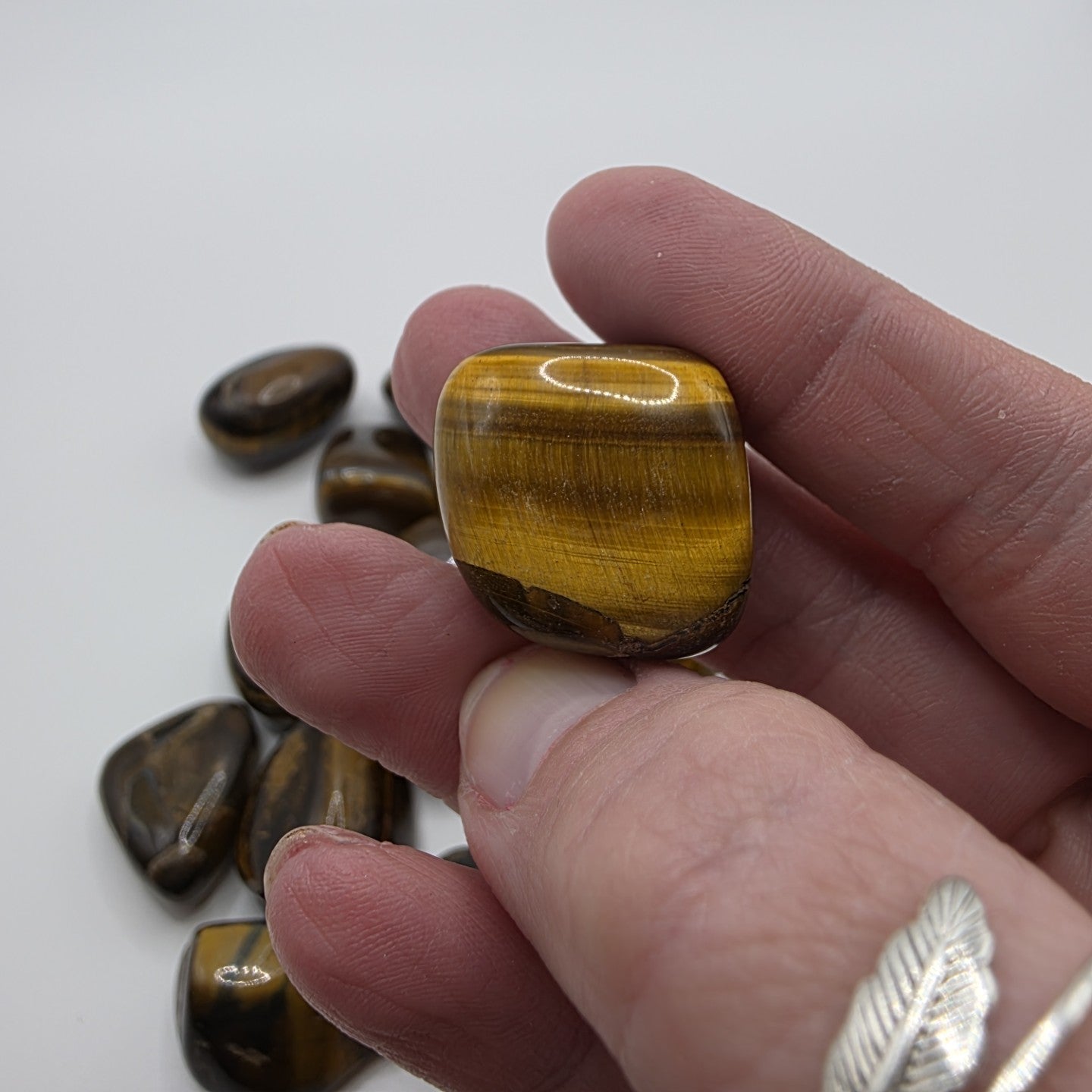 Hand holding a tiger's eye stone with more stones in the background on a white surface