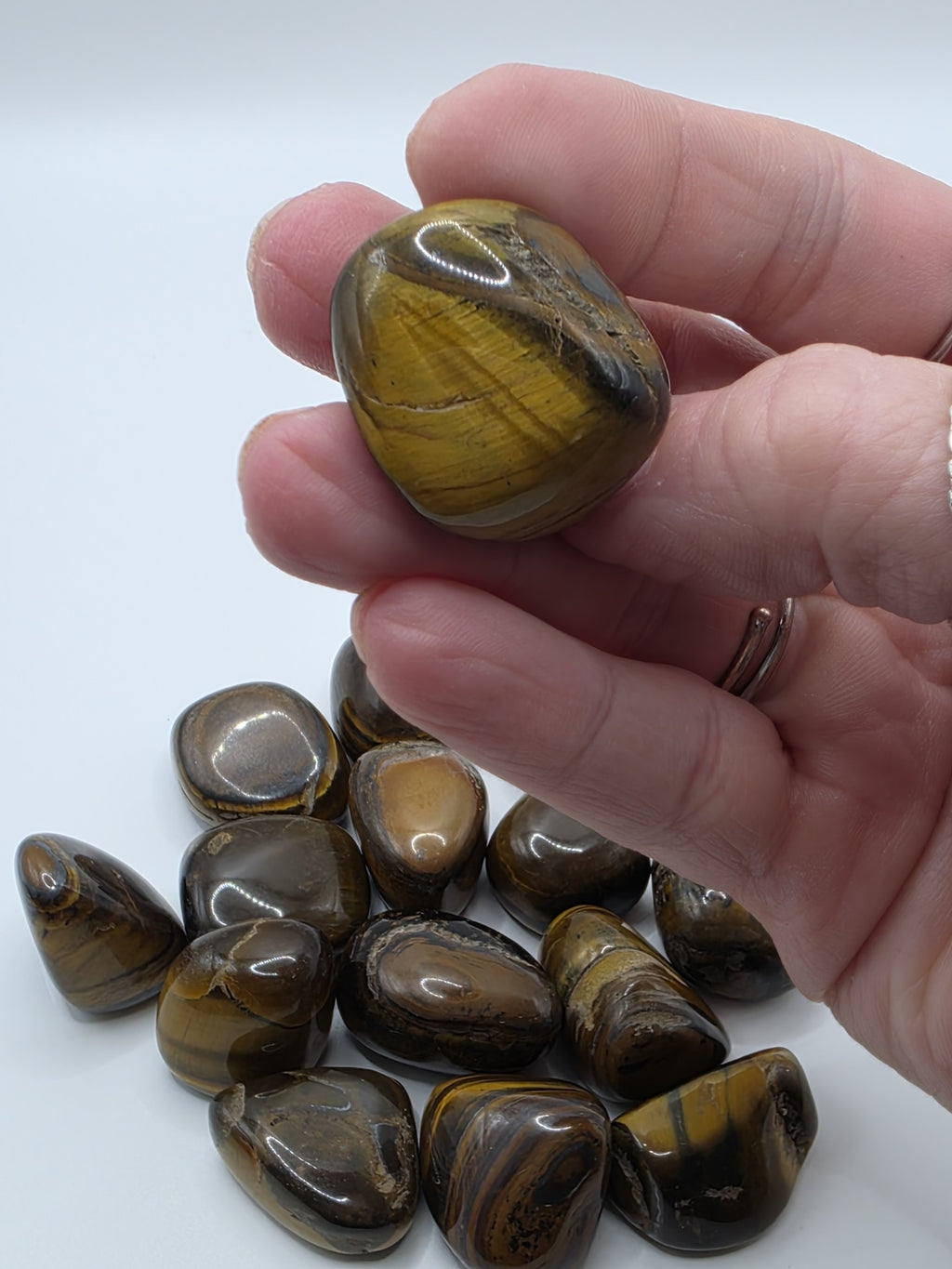 Hand holding a tiger's eye stone with more stones on a white background
