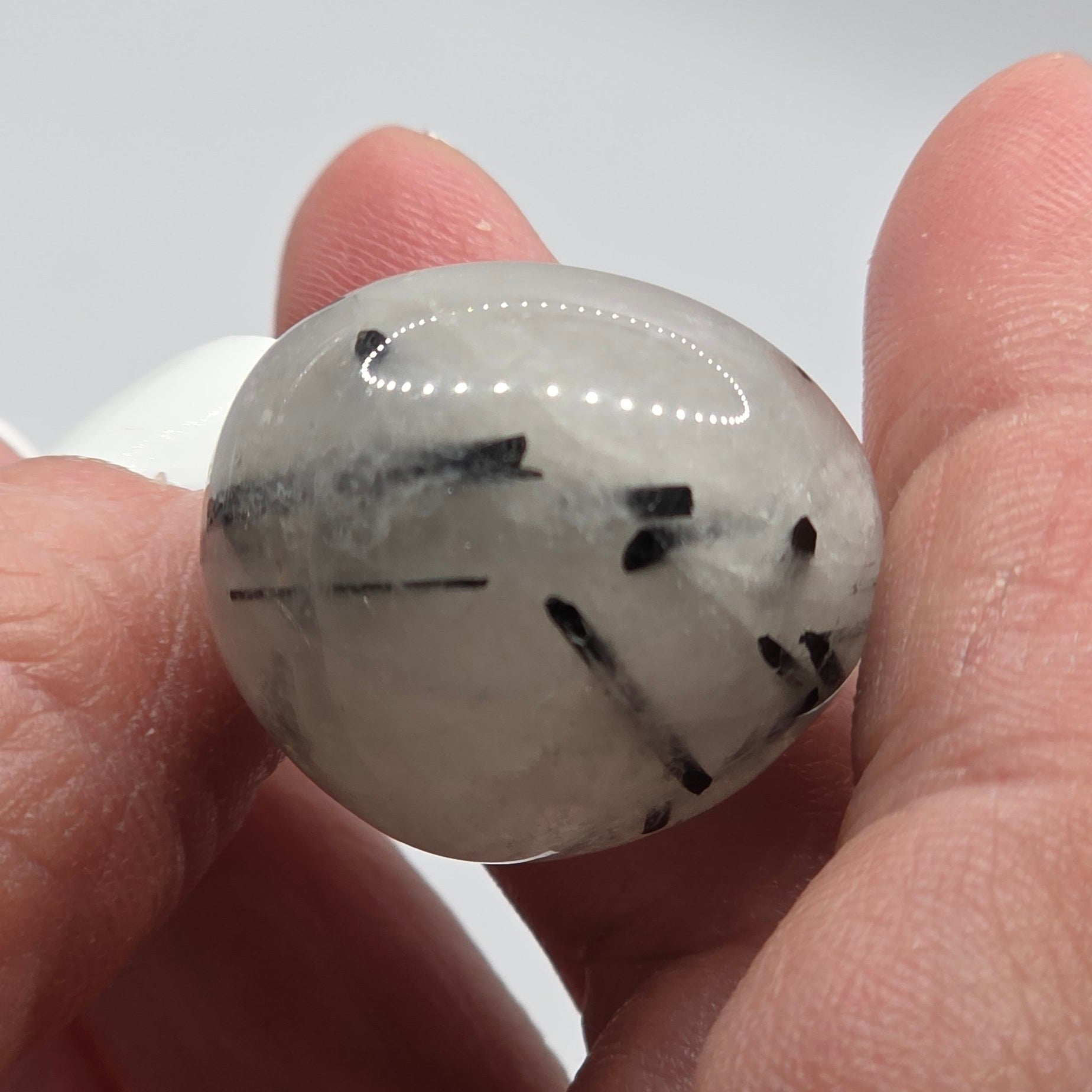 Tourmaline in quartz tumbled stone held in a person's hand showing actual size – clear quartz with black tourmaline needles – 2-3cm polished stone